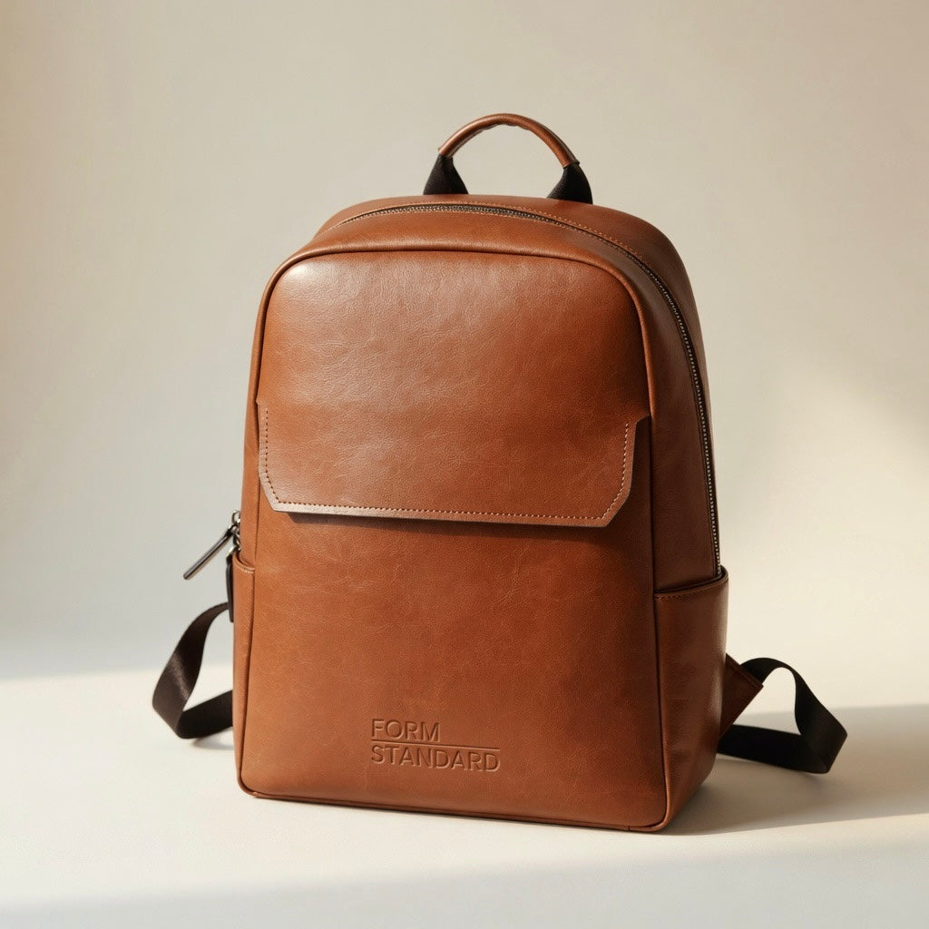 Brown leather backpack with 'FORM STANDARD' branding on a light background
